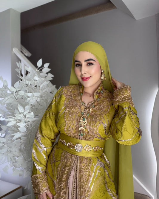 Woman in a green and gold traditional outfit with a matching hijab indoors.